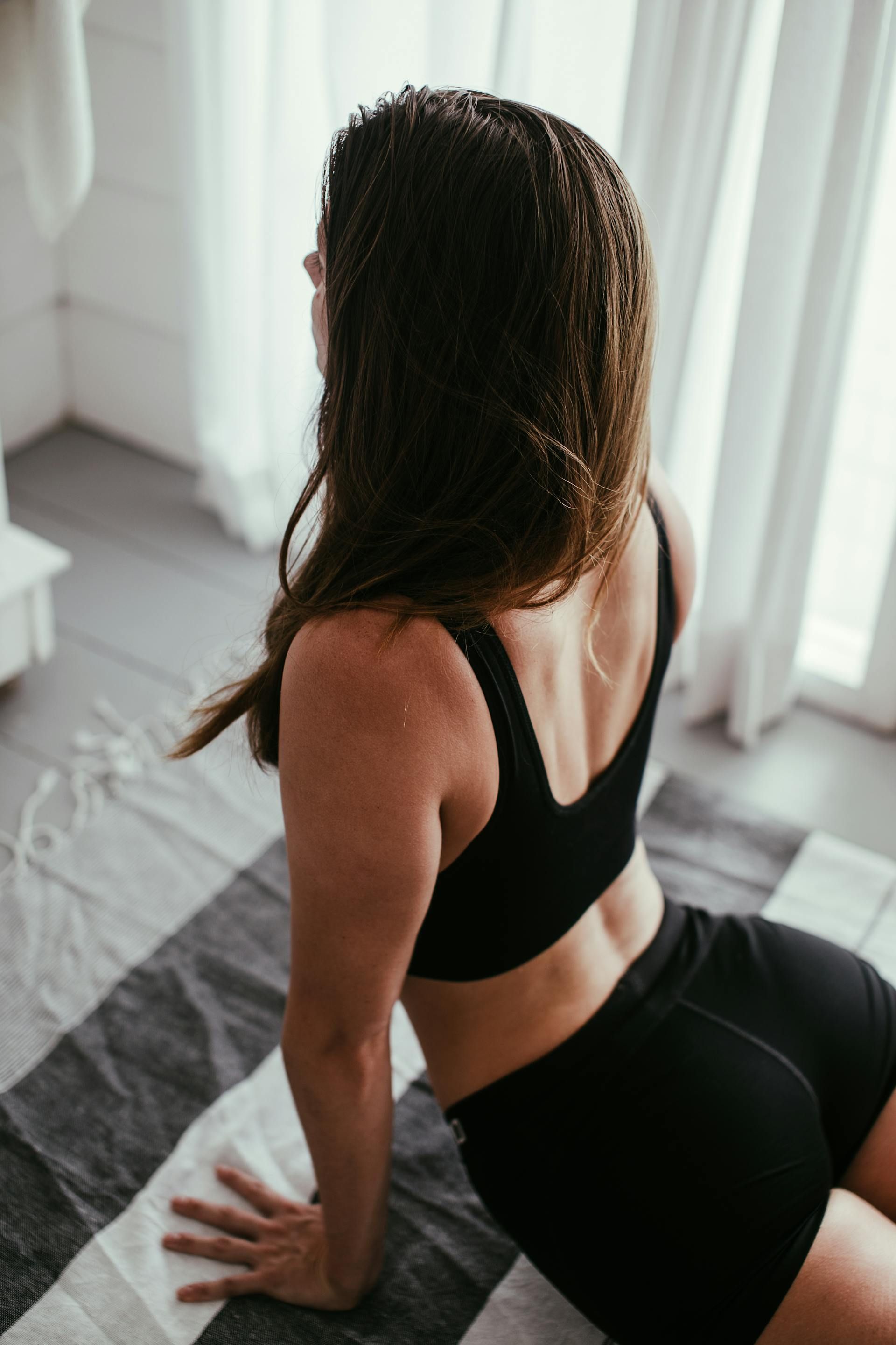 A woman in a black bra and shorts is sitting on a striped rug.