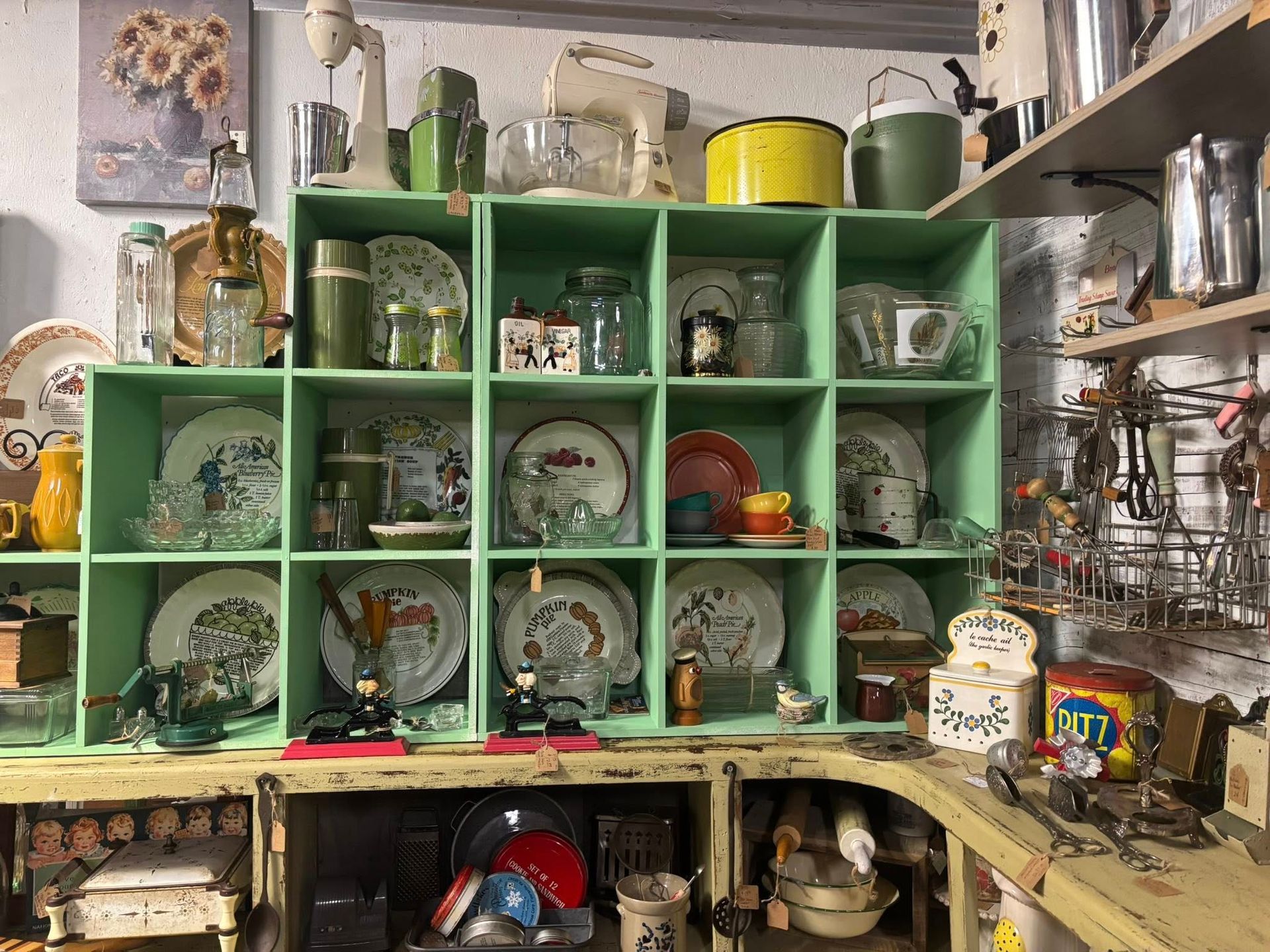 Green cubby shelf displaying vintage dishware and kitchen items.