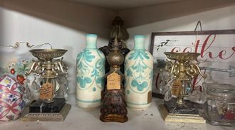 Green gingham bear in rocking chair, holding wooden horse on a light blue table in a shop.
