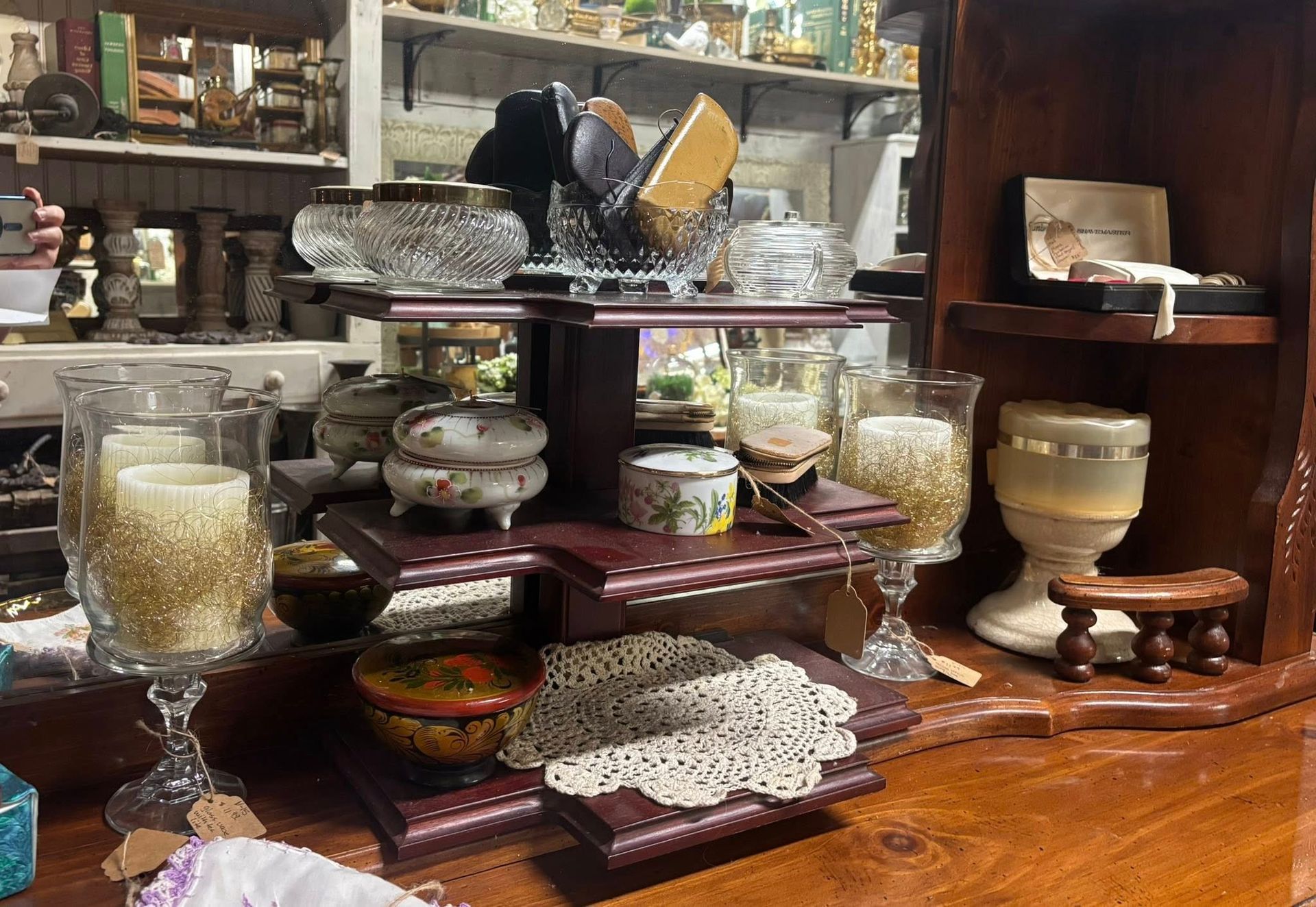 A wooden display shelf with antique objects: candles, bowls, jars, and a jewelry box 