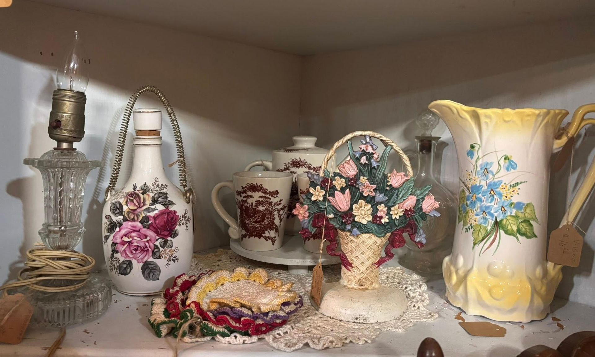 Shelves of antique china and photos in a room with a wooden table holding teacups and a teapot.
