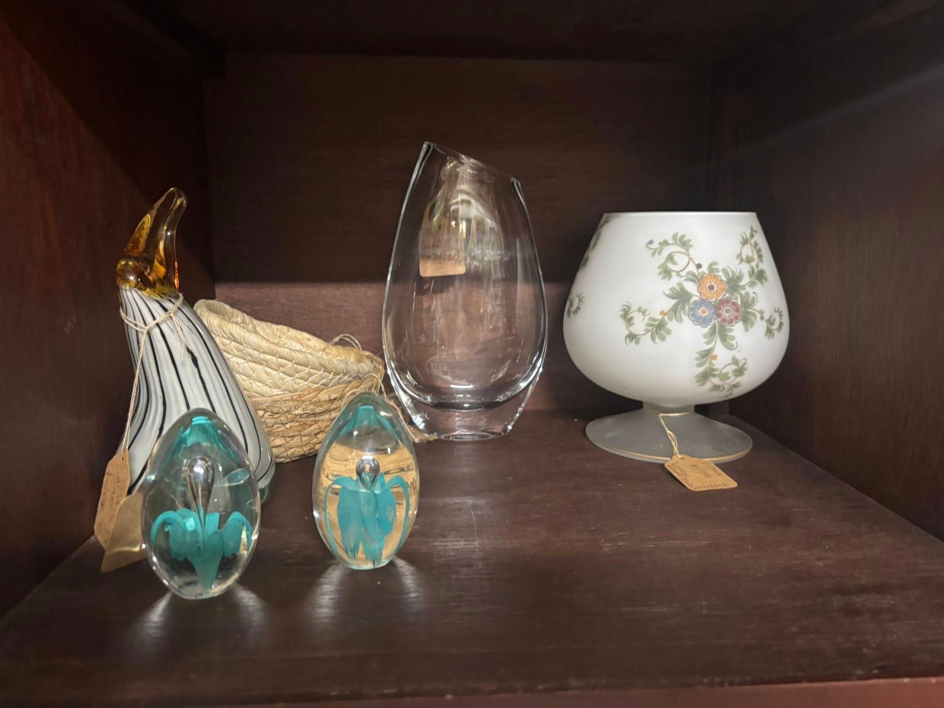 Glass sculptures on a dark shelf: egg, vase, bird, floral globe, and a woven piece.