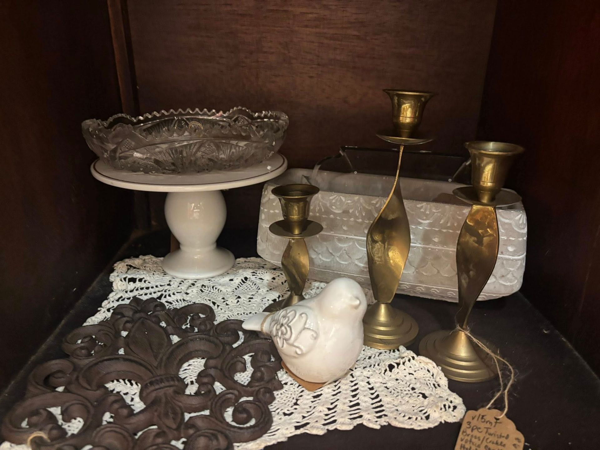 vintage items: glass dish, candlesticks, bird figurine, lace doilies, and fleur-de-lis decoration.