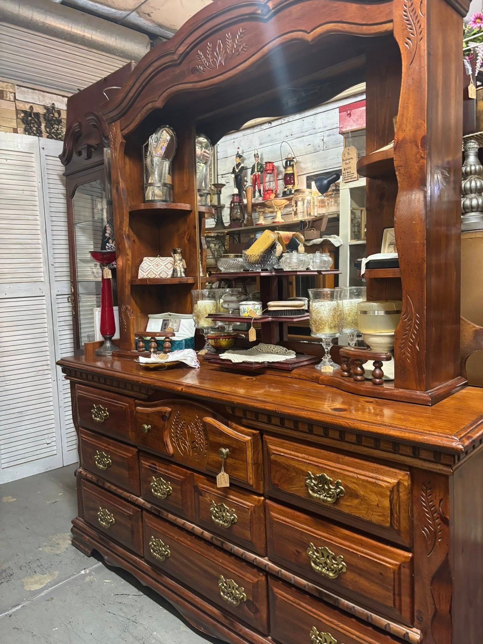 Wooden dresser with mirror and shelves, filled with items. Brown finish, brass hardware.