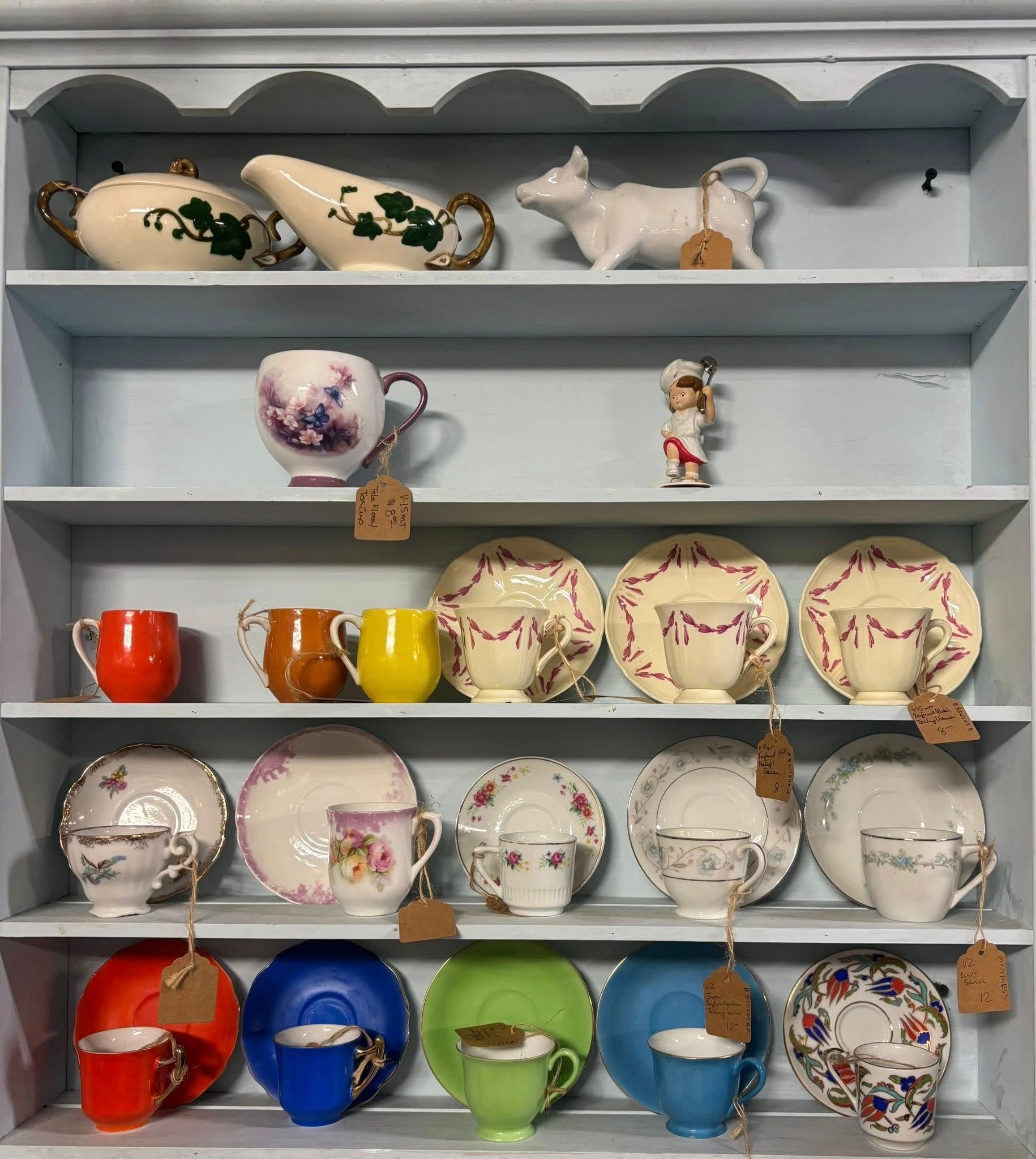 Blue shelf displays various teacups, saucers, and creamers in shades of white, floral patterns, and vibrant colors.