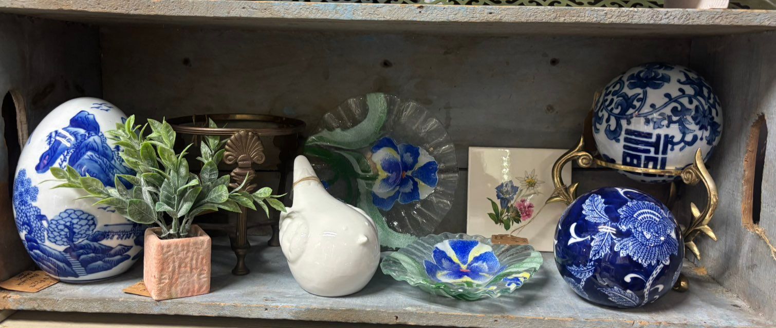 Assortment of blue and white decorative items on a shelf, including eggs, plants, and dishes.