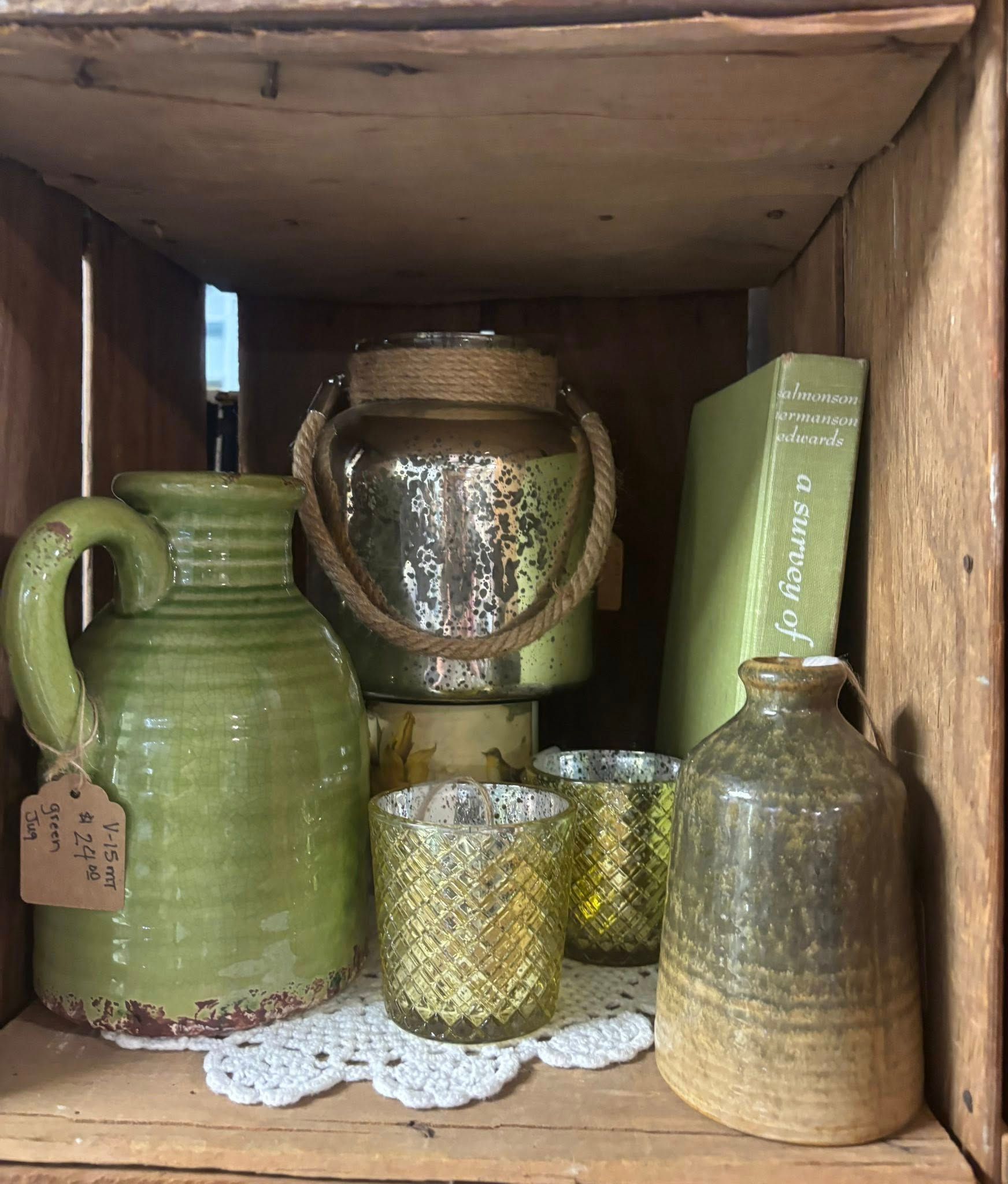 Green and gold decor items in a wooden crate, including a jug, jars, and books.