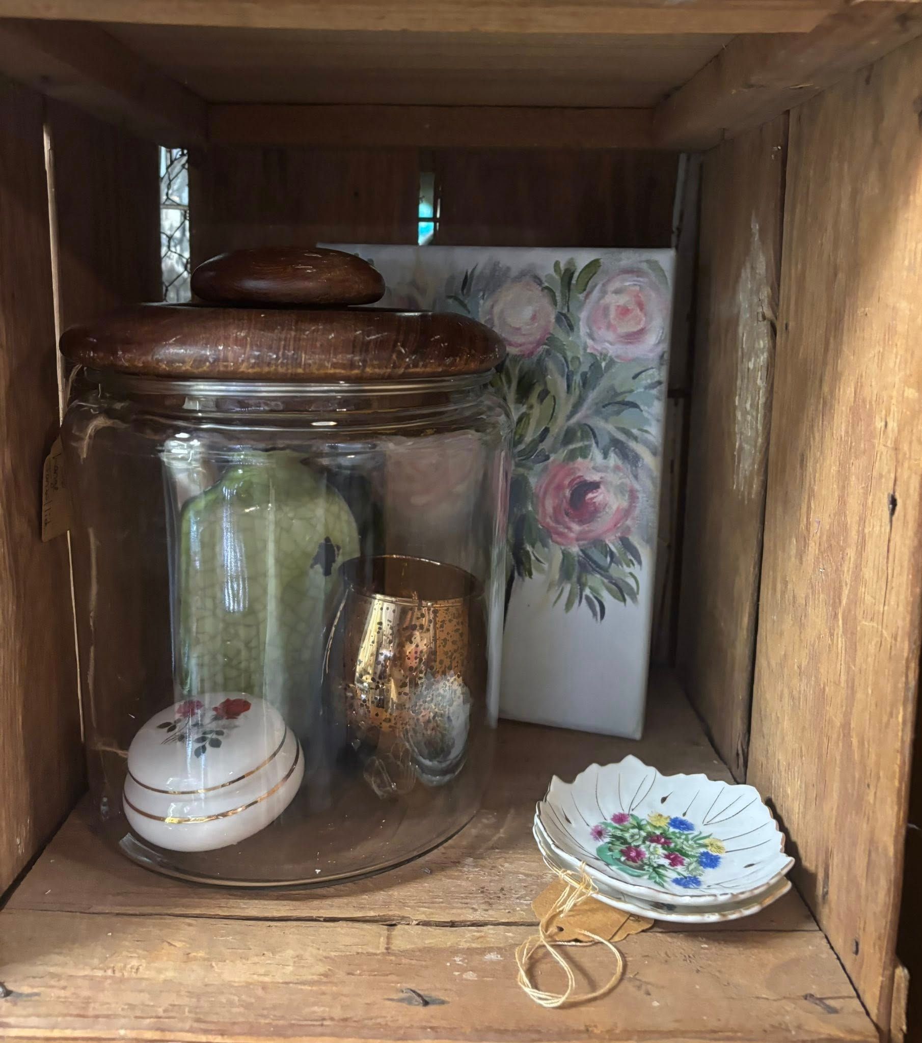 Wooden crate with a glass jar, painting, and small dishes. Browns, greens, and whites.