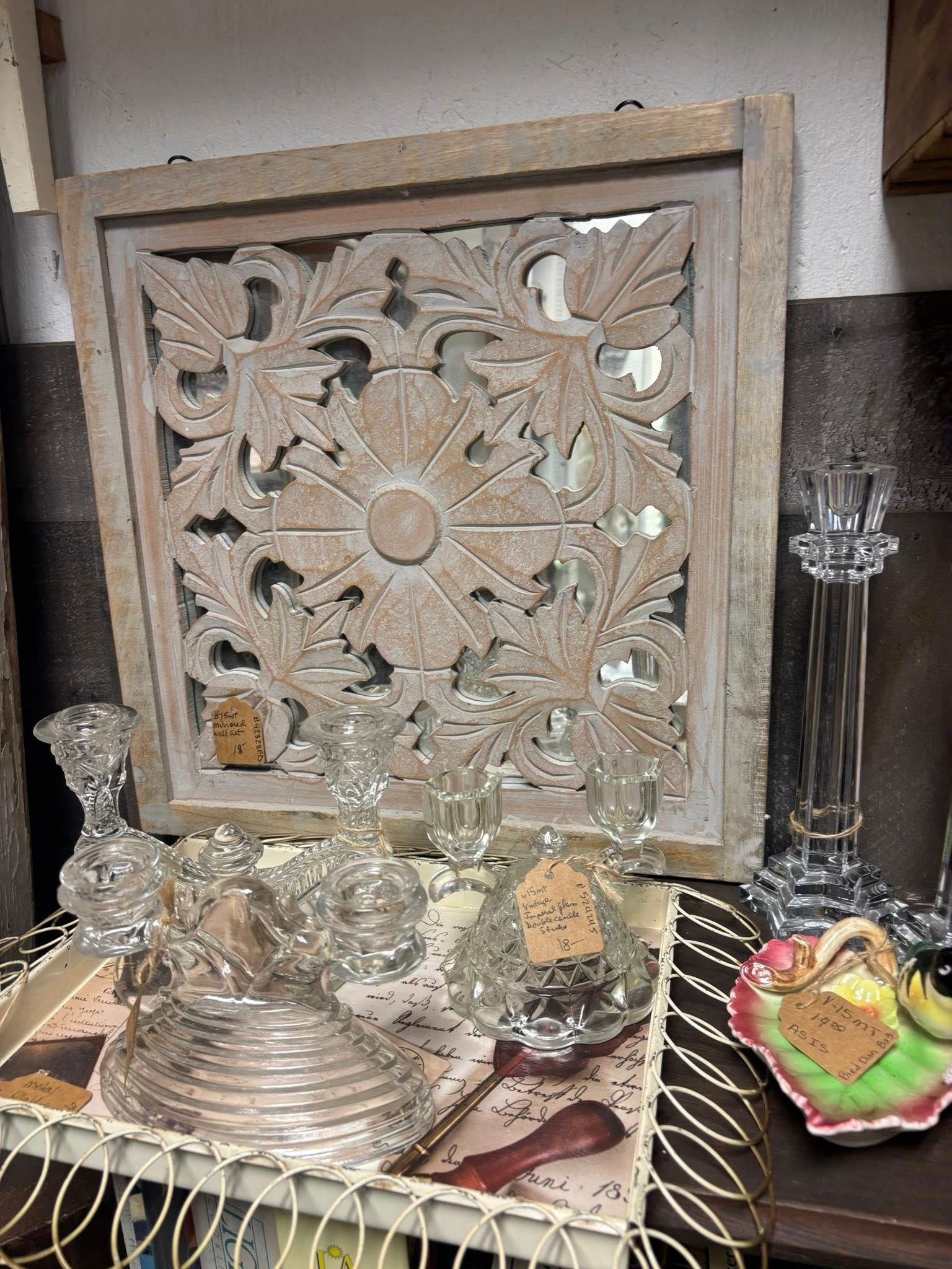 A display of decorative items including carved wooden panel, glass candlesticks, and various trinkets on a shelf.