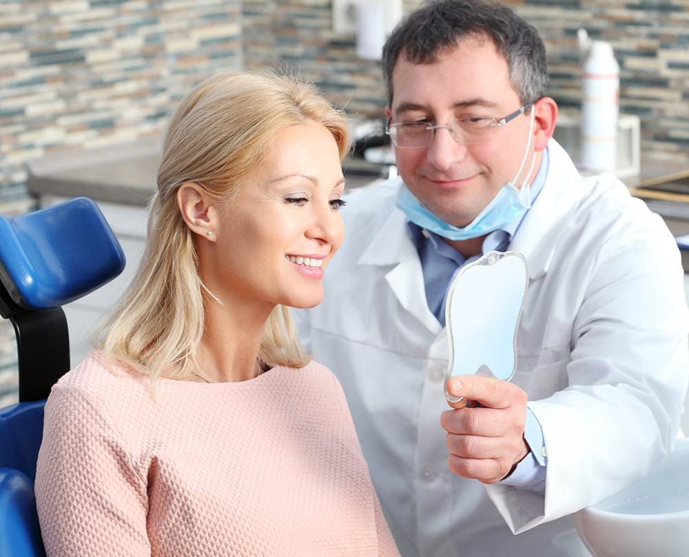 A dentist is looking at a woman 's teeth in a mirror.
