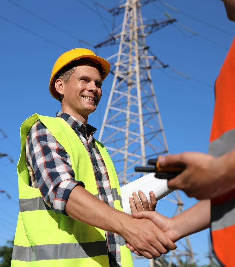 Two men shaking hands in front of a power tower