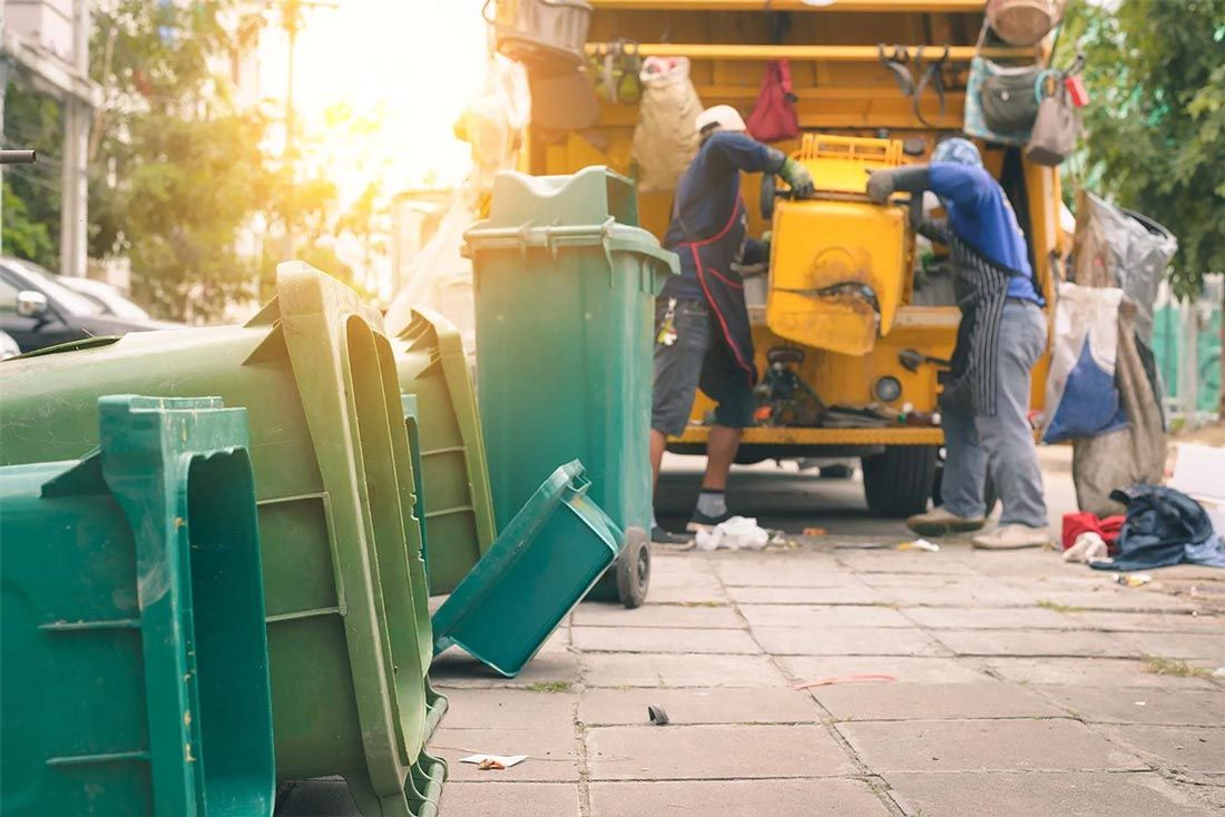 A group of people are loading garbage into a garbage truck.