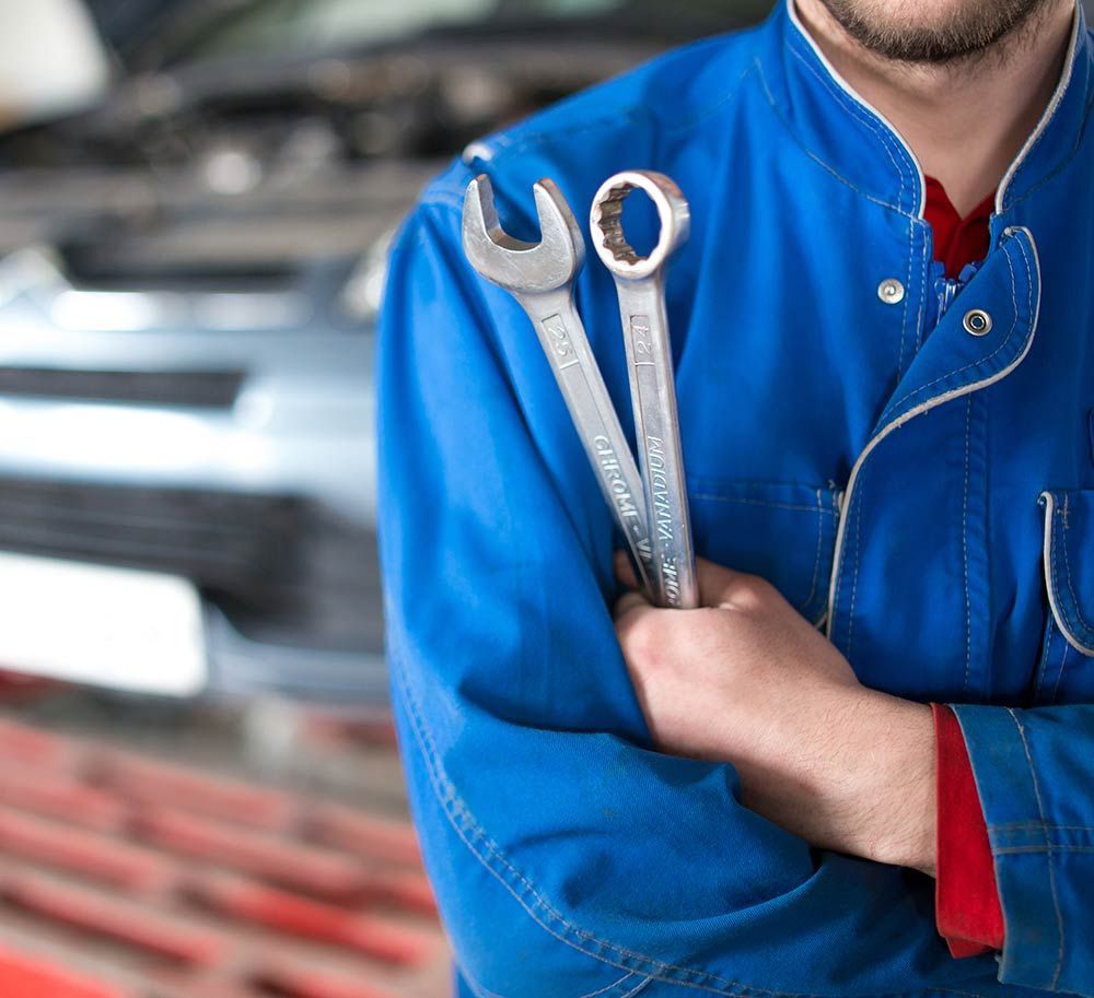 A man in a blue jacket is holding two wrenches in his hands