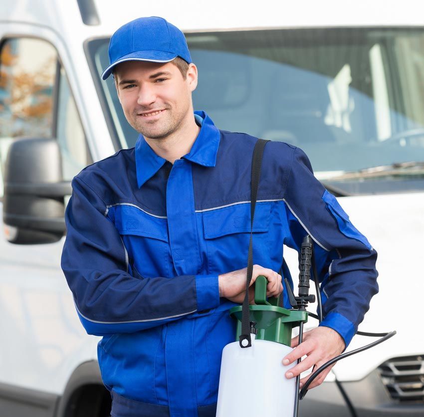 A man in a blue uniform is holding a sprayer in front of a white van