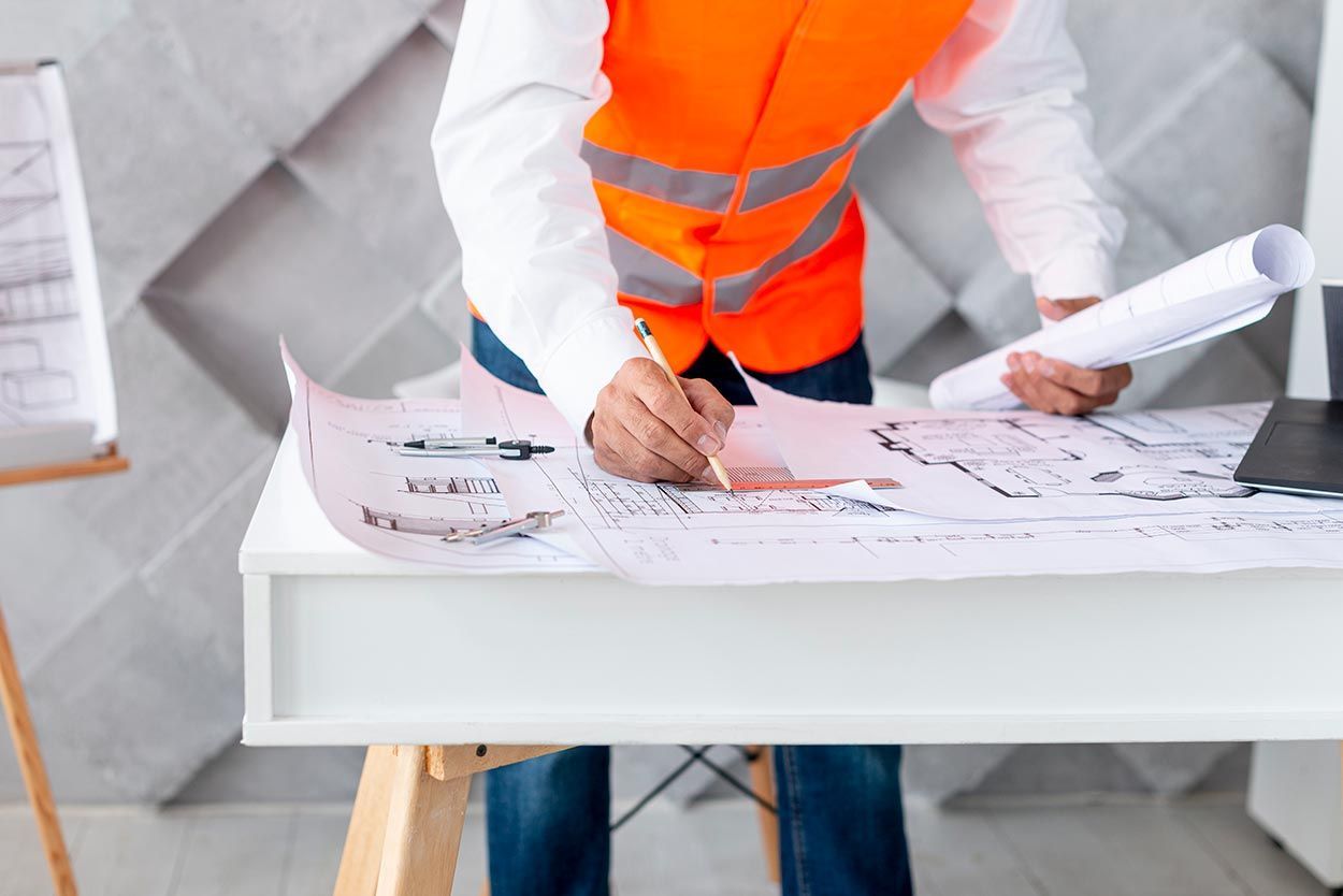 A man in an orange vest is sitting at a desk writing on a piece of paper.