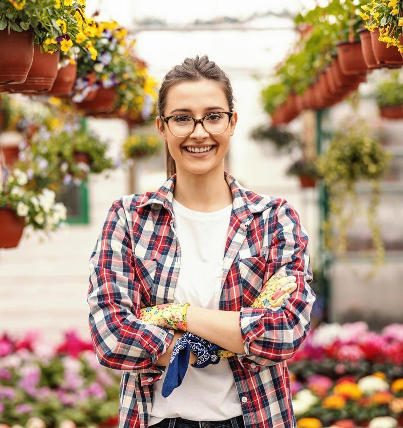 A woman is standing in a garden with her arms crossed and smiling.