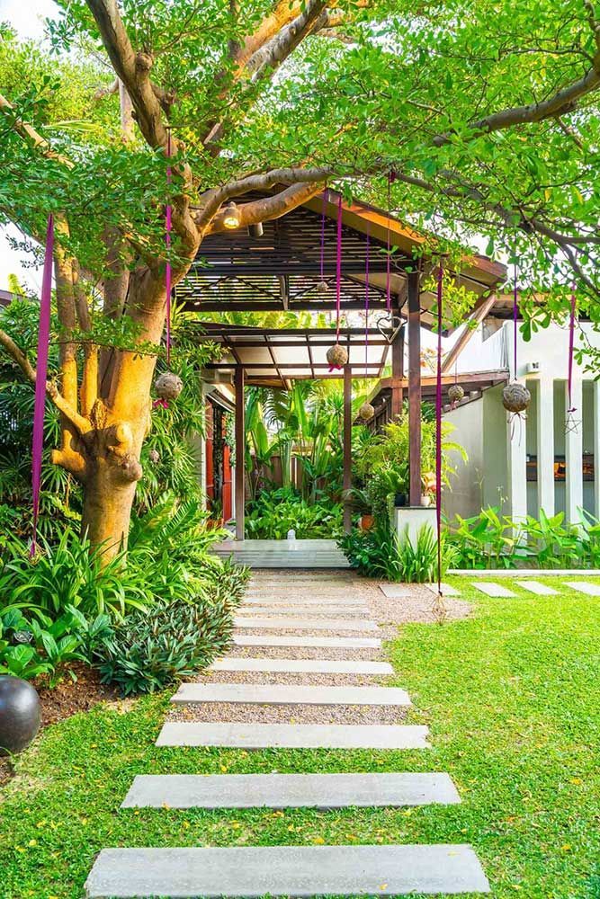 A stone walkway leading to a house in a lush green garden.