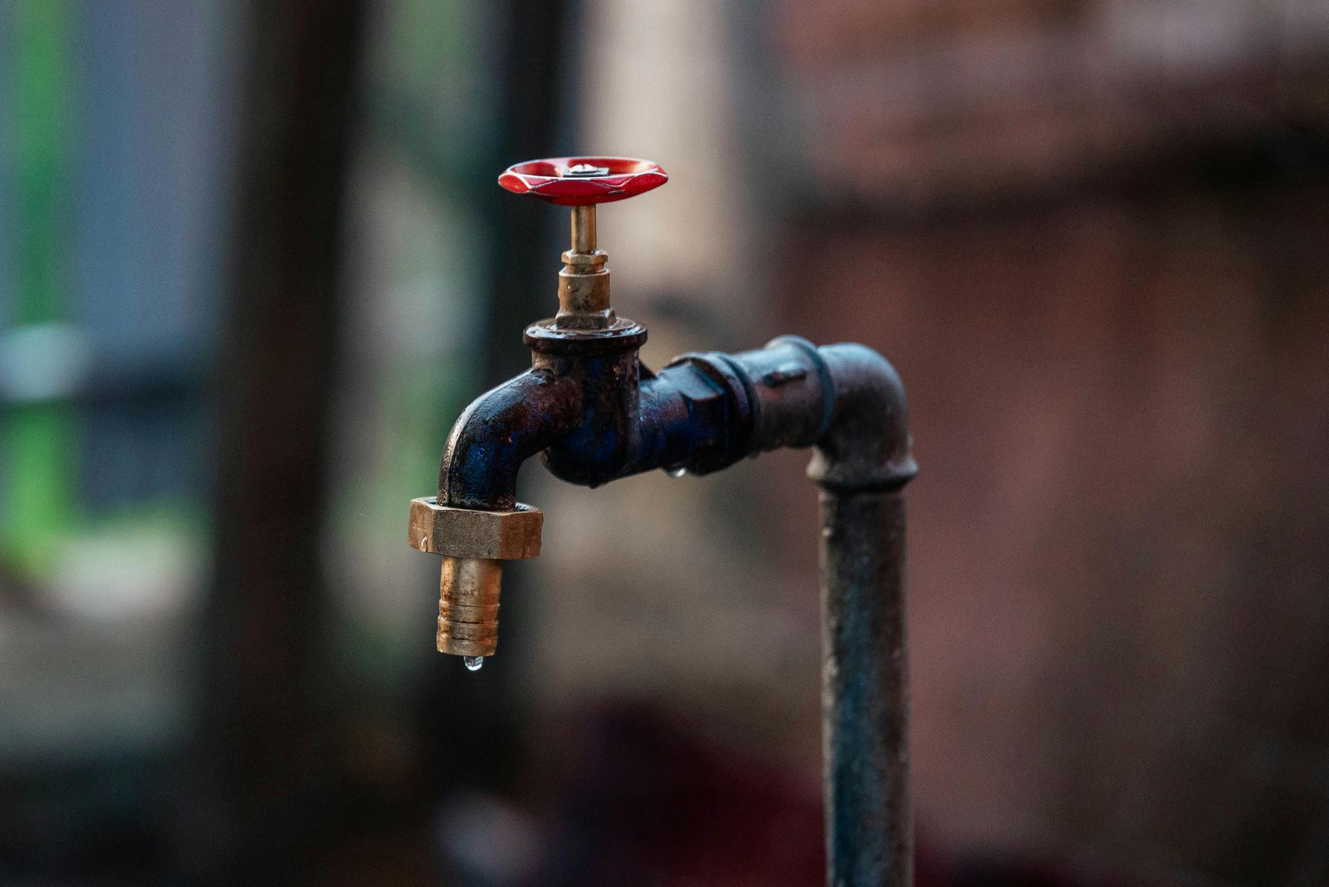 Rusty outdoor faucet with a red handle and a single water drop.