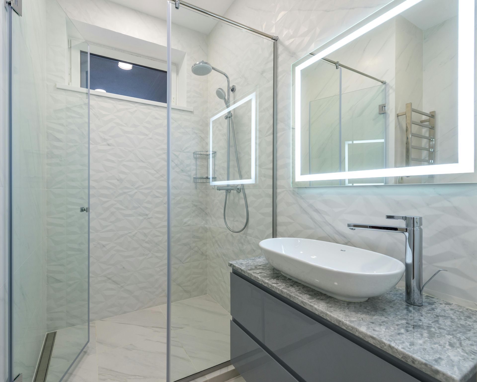 Modern bathroom with a glass shower, vanity sink, and backlit mirror.