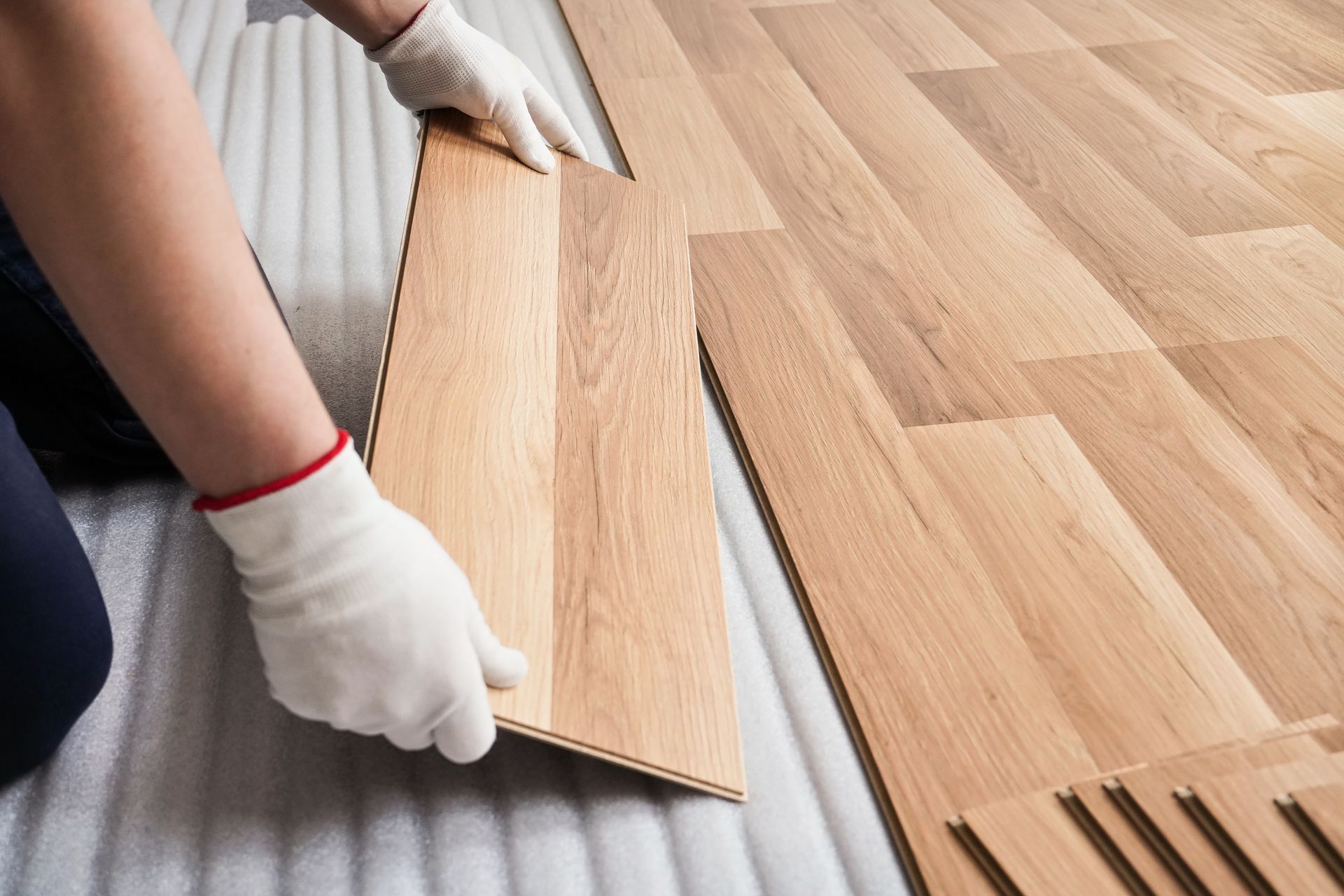 Installer aligns wood planks while laying new laminate flooring over padded underlayment.