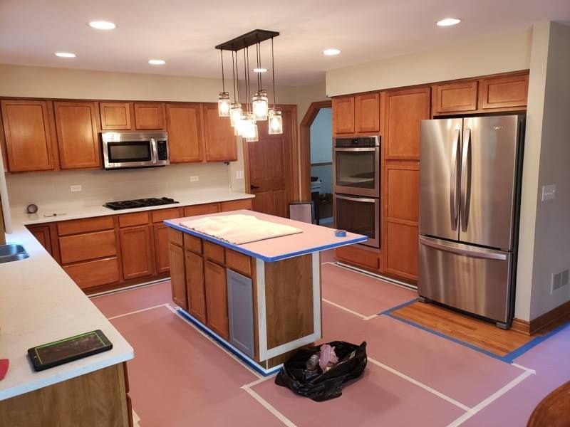 Modern kitchen with wooden cabinets, stainless steel appliances, and an island under construction with blue tape markings