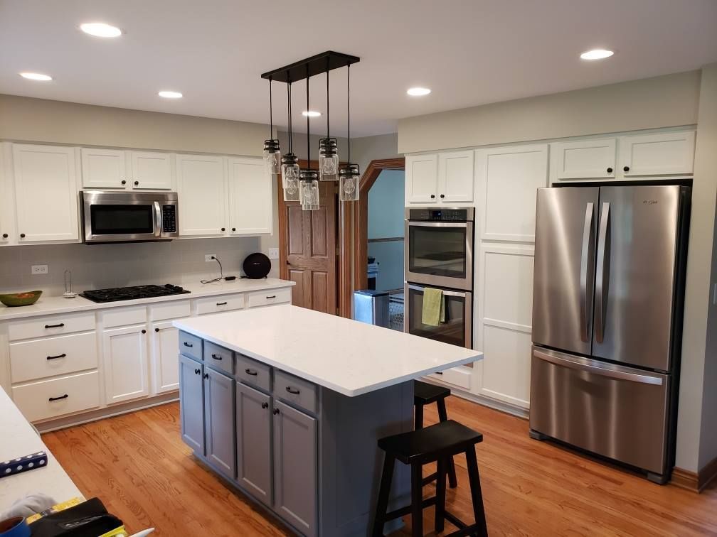 Bright modern kitchen with white cabinets, stainless steel appliances, and a gray island with stools