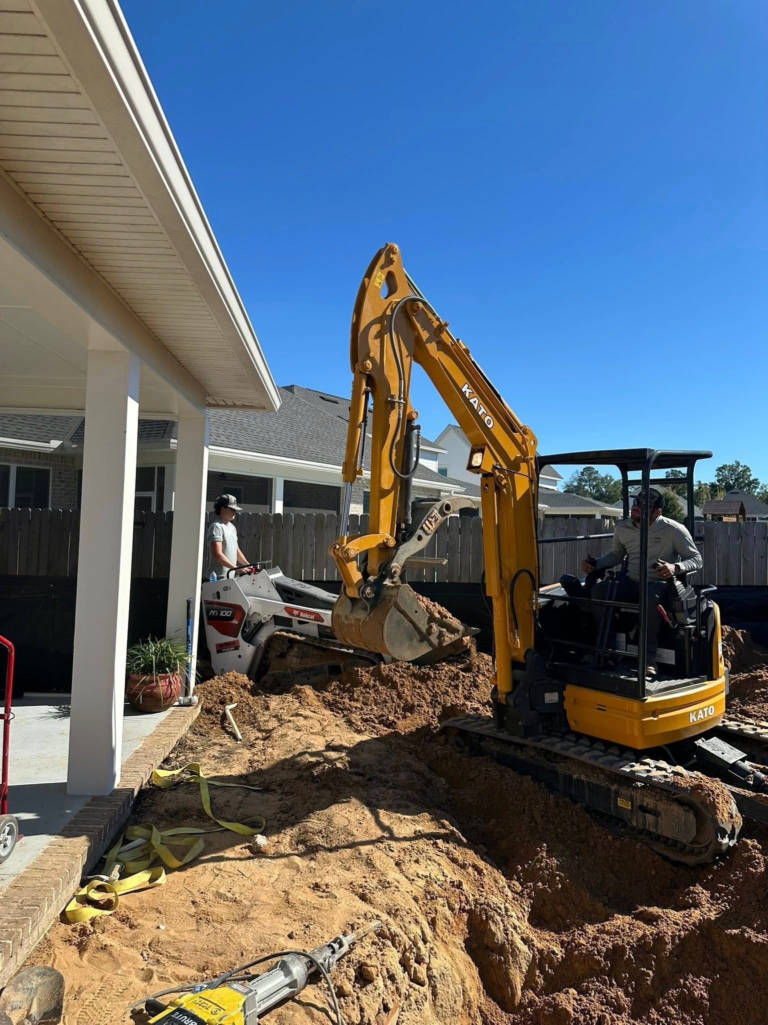 Yellow excavator digging dirt near a white building under a blue sky.