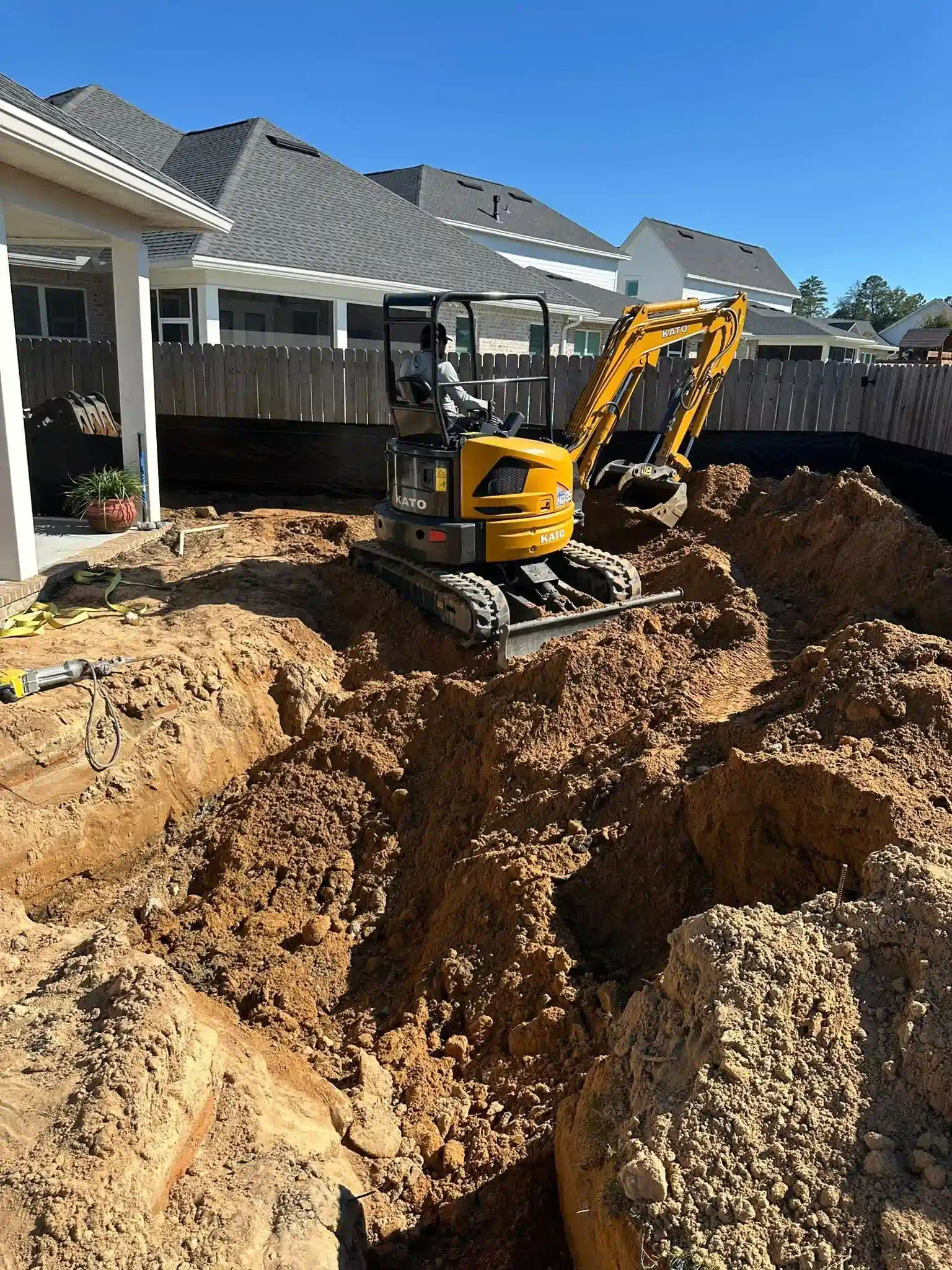 Yellow excavator digging in a dirt pit near a house.
