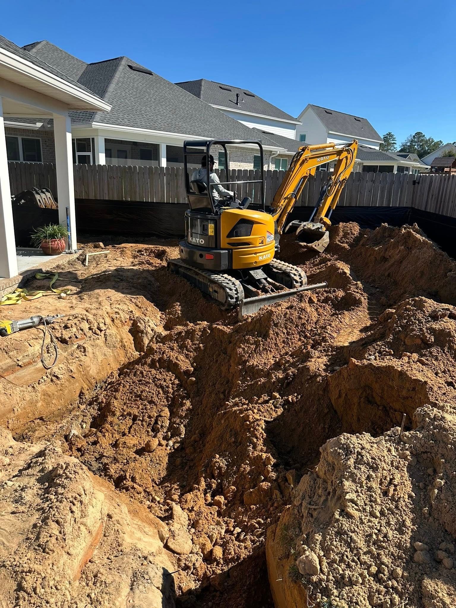 Yellow excavator digging in a dirt pit near a house under a clear sky.