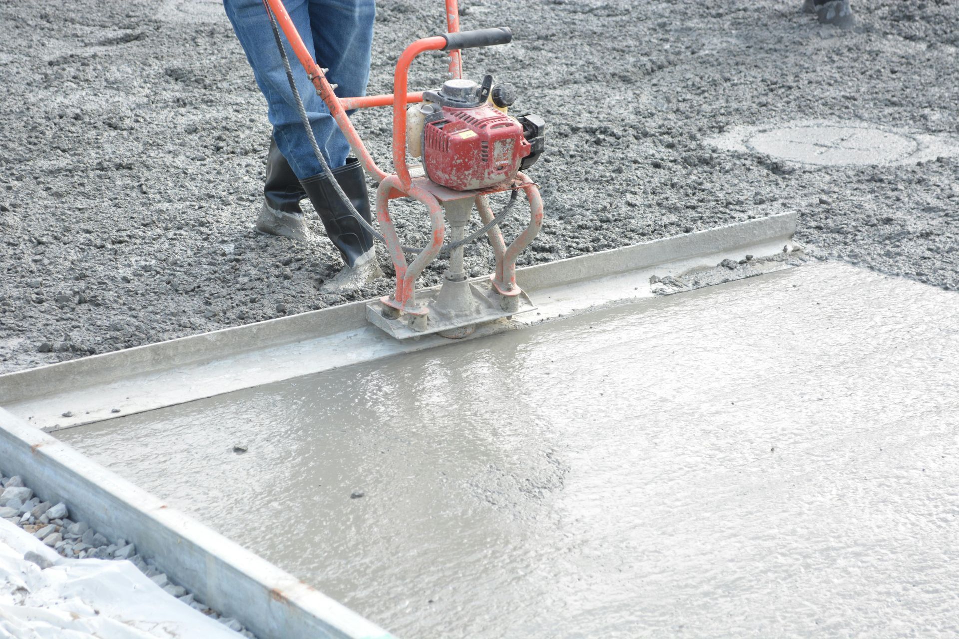 Worker using a concrete vibrator to smooth wet concrete on a slab