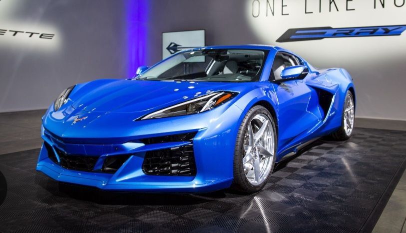 A blue sports car is on display in front of a sign that says one like no