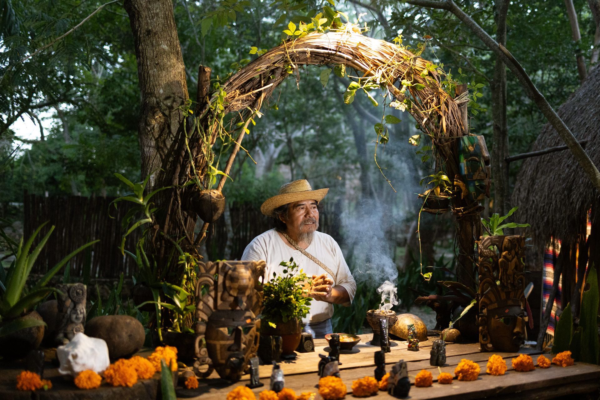 A man in a straw hat is sitting at a table in the woods.