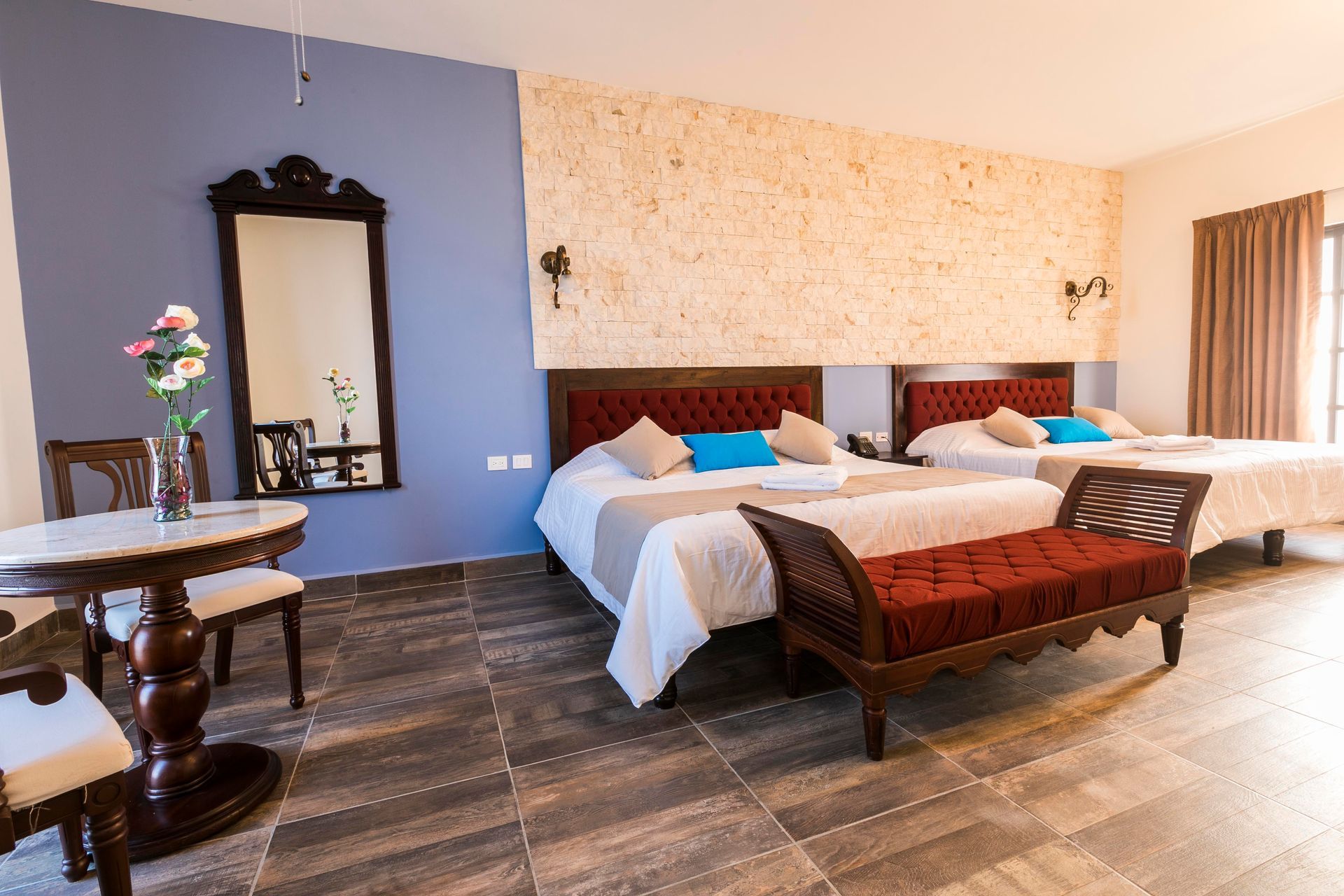 A hotel room with three beds , a table , chairs and a mirror.