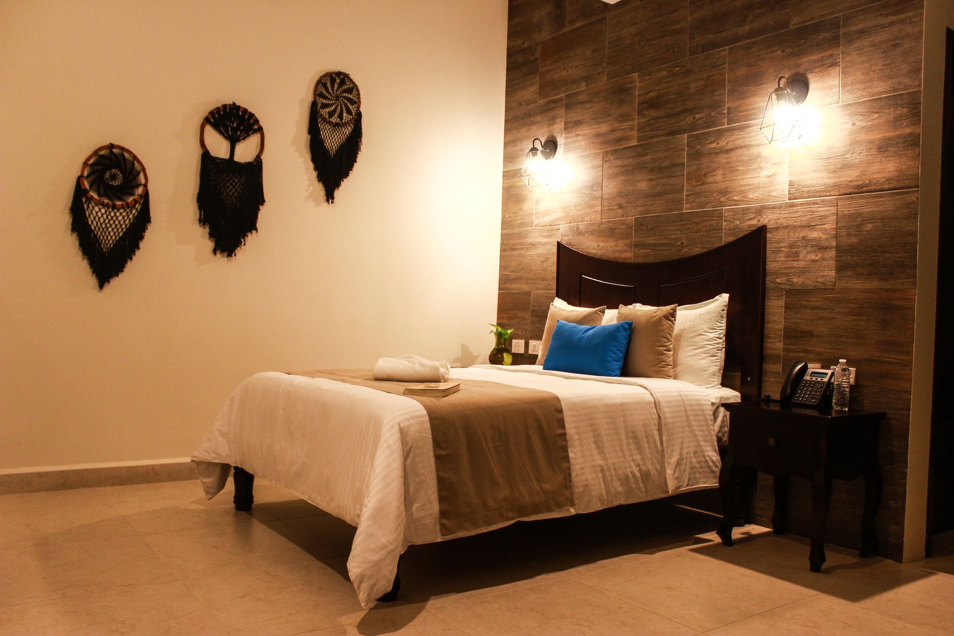 A hotel room with a bed , nightstand , and masks on the wall.