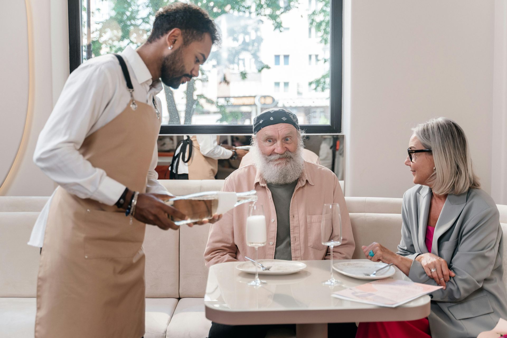 waiter serving an elder gentleman and his spouse in a restaurant during the day time