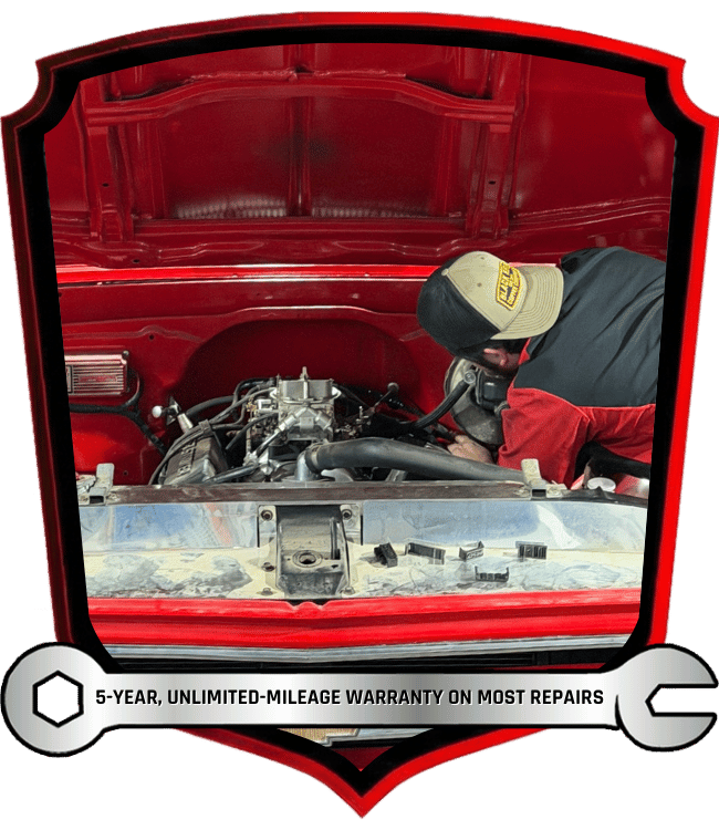 Technician working inside classic truck engine bay during transmission and drivetrain repair