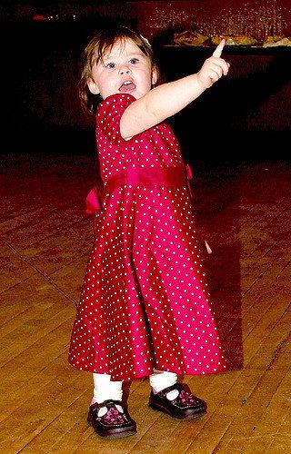 A little girl in a red polka dot dress is pointing up