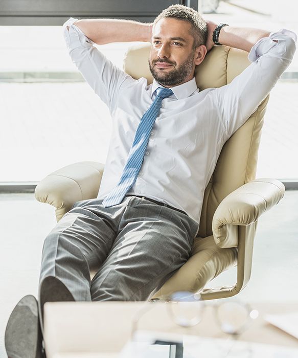 A man is sitting in a chair with his hands behind his head.