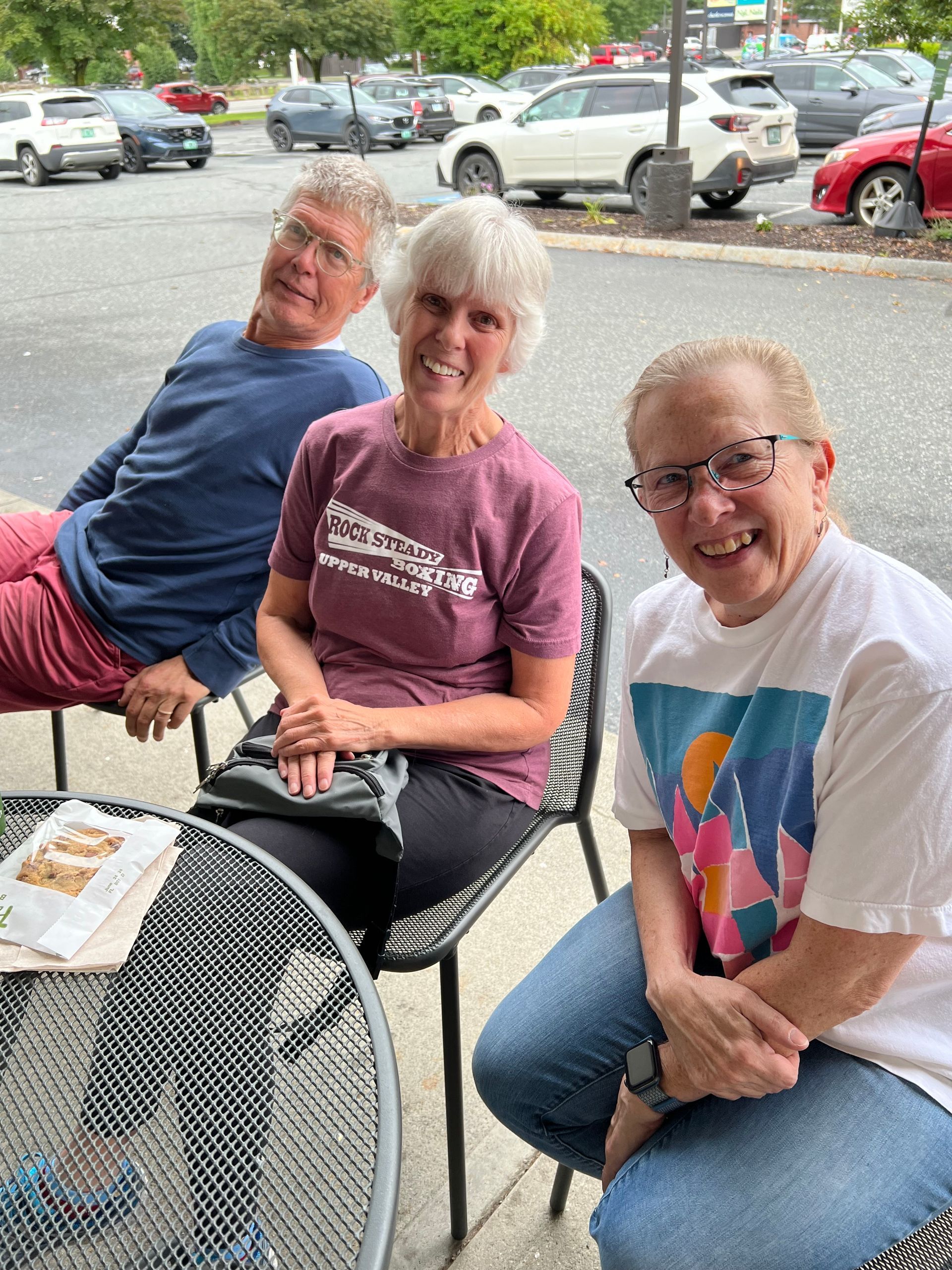Three people are sitting at a table in a parking lot.