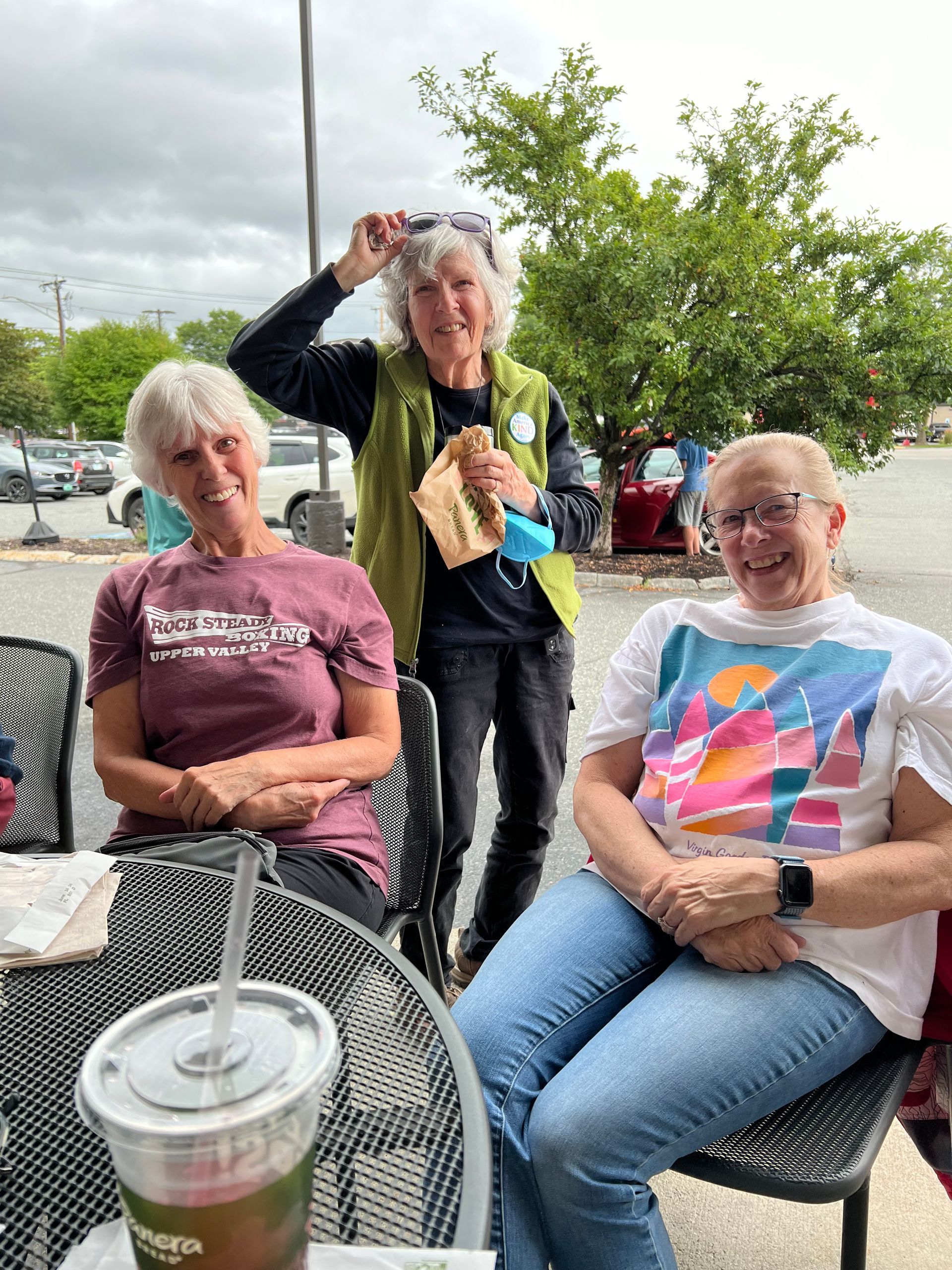 Three older women are sitting at a table with a drink.