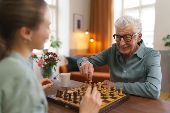 An elderly man and a young girl are playing a game of chess.