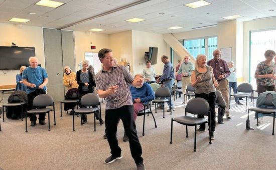 A group of people are dancing in a room with chairs.