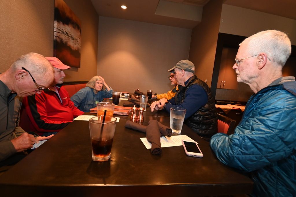 Three people are sitting at a table in a parking lot.