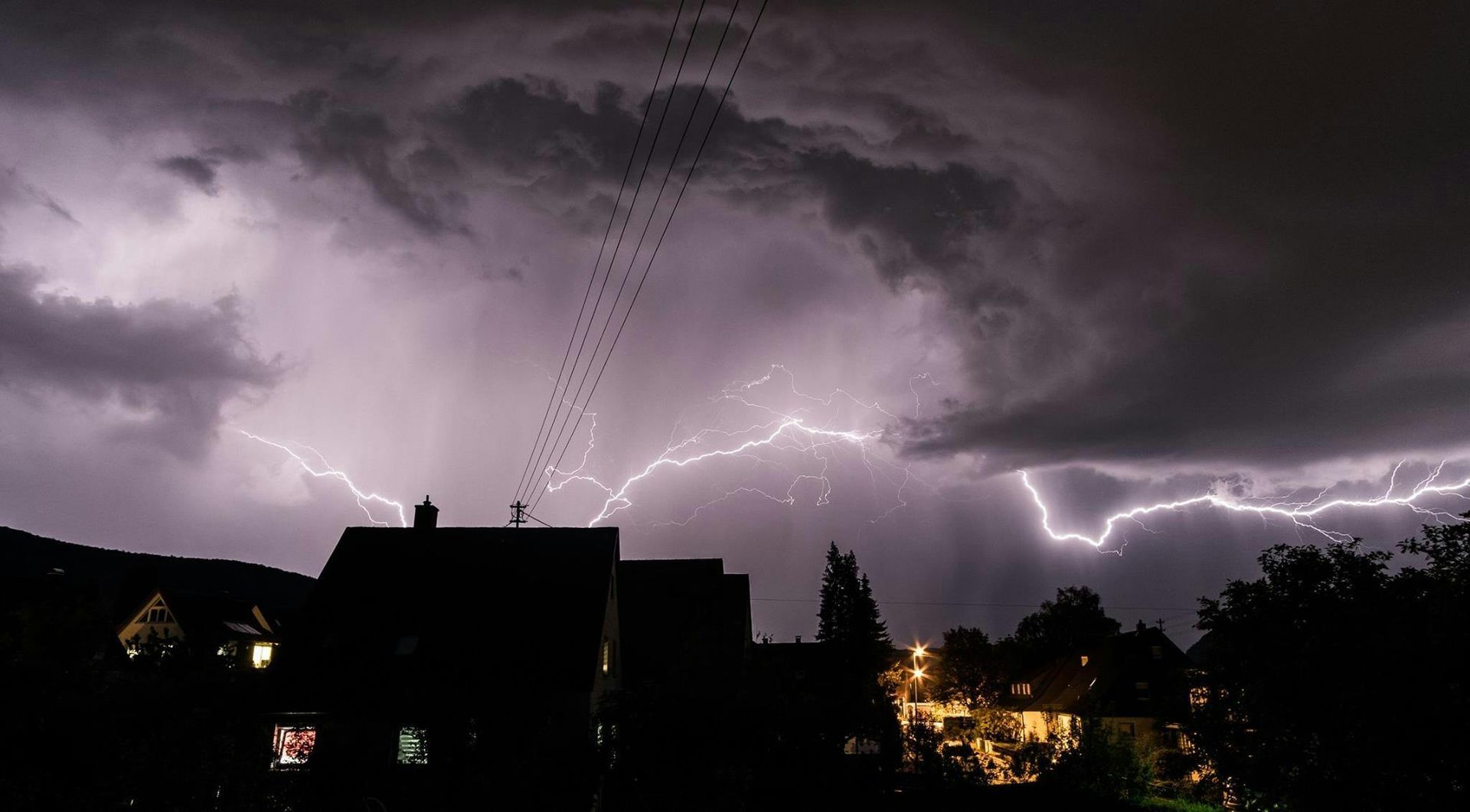 A lightning storm is coming over a city at night.