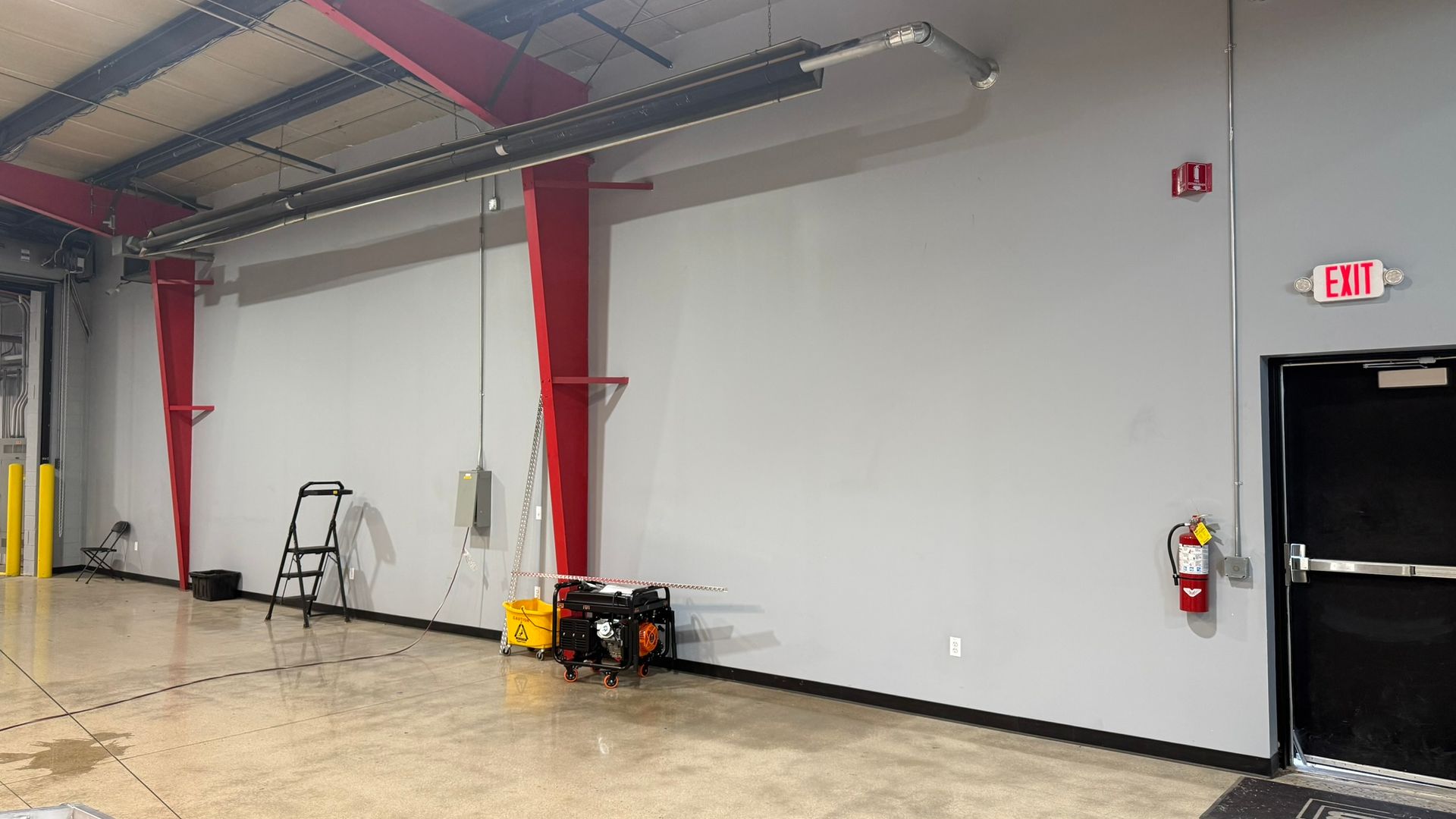 A large empty room with a fire extinguisher on the wall.