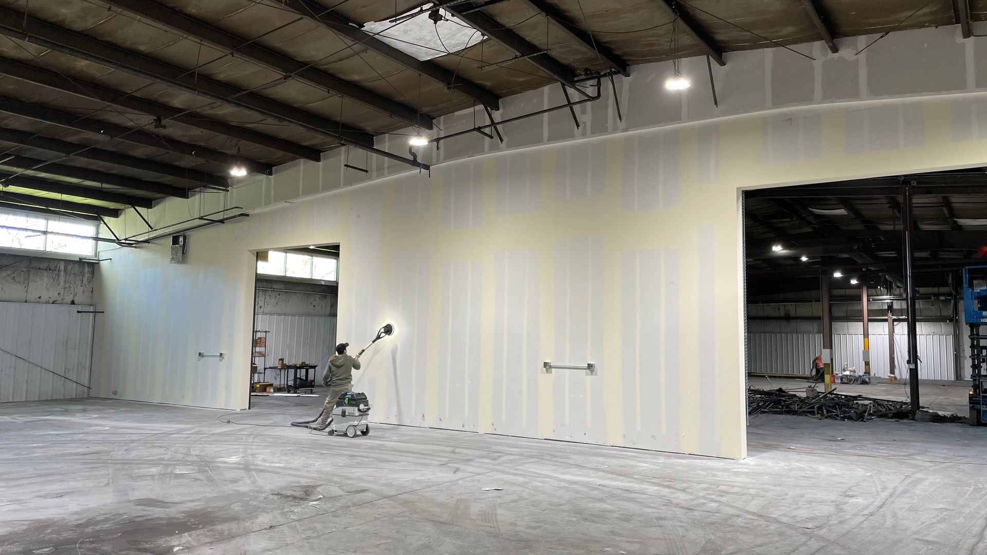 A man is painting a wall in a large warehouse.