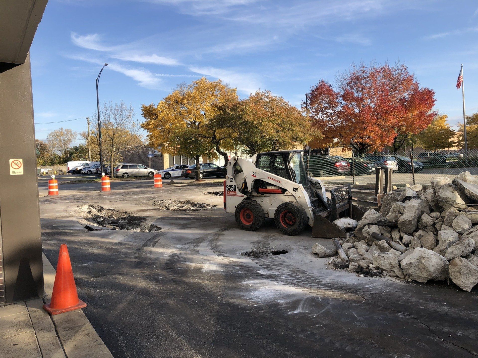 A bobcat is moving a pile of rocks in a parking lot.