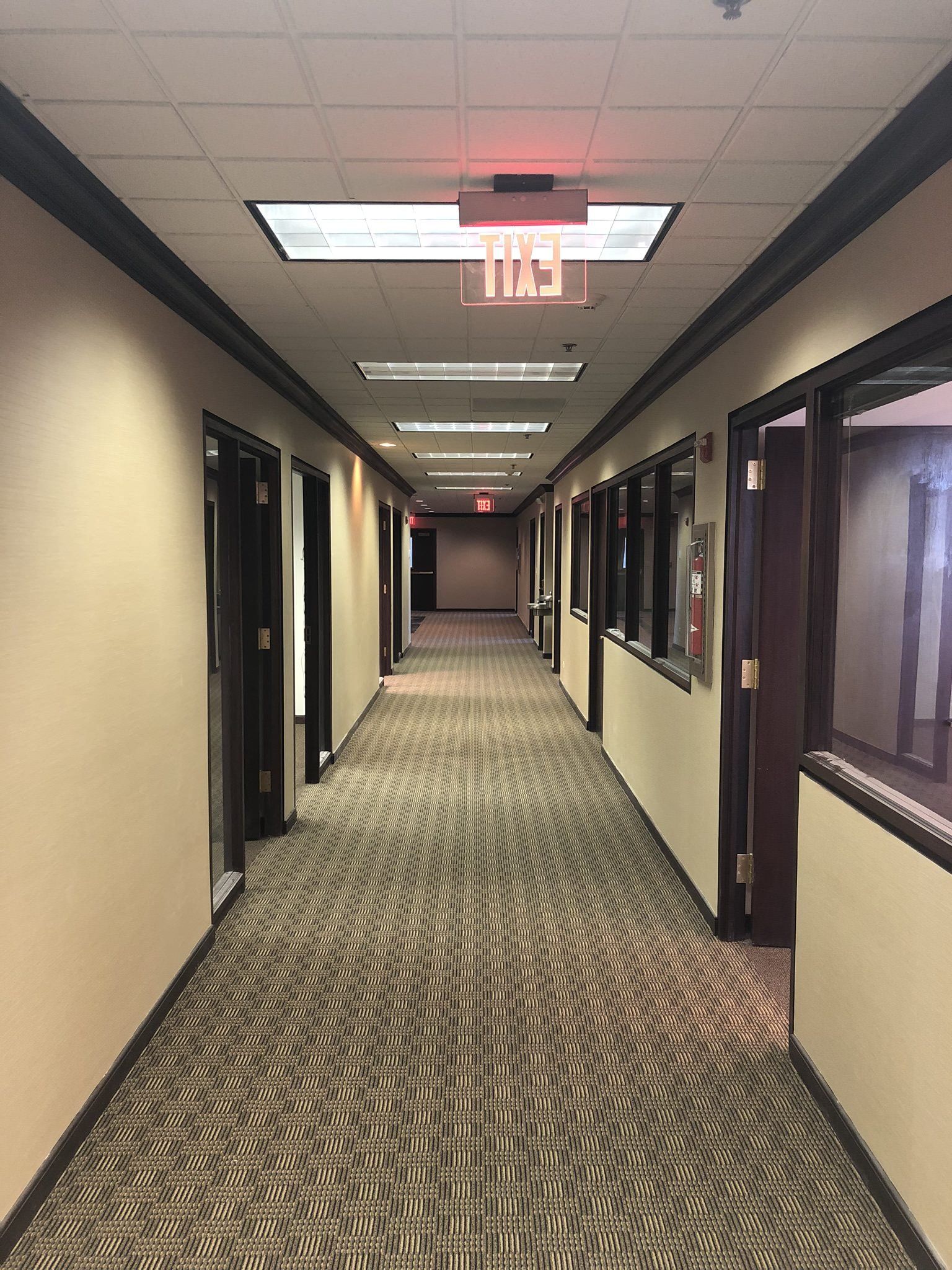 A long hallway with a red exit sign on the ceiling.