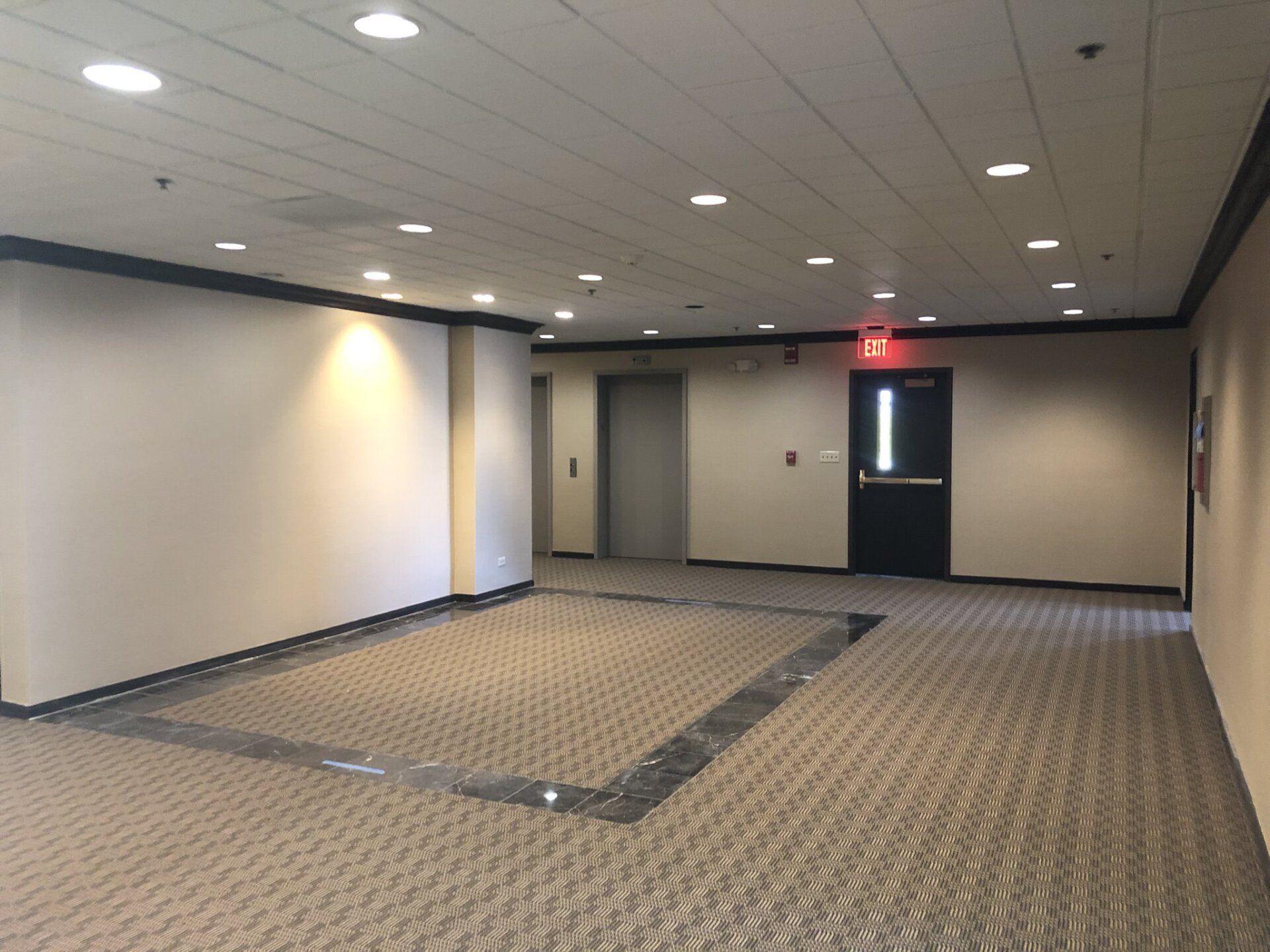 An empty hallway with a red exit sign on the door