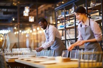 A man and a woman are setting tables in a restaurant.